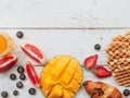 Flat lay summer breakfast with waffle and fruits. Frame mockup with mango, strawberry, and cherry on wooden background