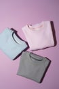 Flat lay of three folded pastel pink, blue and gray sweatshirts isolated on pale purple background Royalty Free Stock Photo