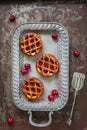 Flat lay of three individual cherry pies and fresh cherries on a serving tray on rustic background Royalty Free Stock Photo