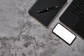 Flat lay, top view of black spiral notebook ,pen, laptop and smartphone with blank white screen on modern concrete loft desk Royalty Free Stock Photo