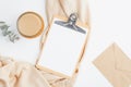 Flat lay, top view female cozy table desk with clipboard mockup, cup of coffee, envelope, beige blanket and eucalyptus flower.