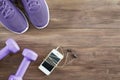 Flat lay top view Fitness accessories on a wood background. Smart phone, purple dumbbells, purple running shoes, ear phone.