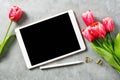 Flat lay top view mockup: digital tablet with pencil and red tulips on grey background. Copy space