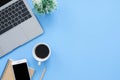 Flat lay top view mockup photo of working space with laptop, smartphone, coffee up and notebook on blue pastel background.