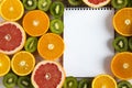 Flat lay Top view notebook with sliced kiwi, orange, grapefruit and mandarin on light wooden background. Royalty Free Stock Photo