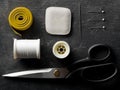 Flat lay top view sewing tools with measurement tape, chalk, thread, needles and scissors on black dark wood table