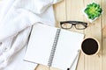 Flat lay or top view of white knitted blanket, eyeglasses, cup of coffee and blank notebook paper on wooden background Royalty Free Stock Photo