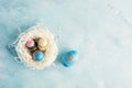 Flat lay top view white paper nest with three vintage Easter eggs and one blue egg with red heart on blue background Royalty Free Stock Photo