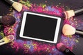 Flat lay of touchpad with blank screen with makeup brushes on colorful background of crumbled eyeshadows