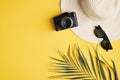Flat lay traveler accessories on yellow background. Top view female beach hat, vintage camera, sunglasses, palm leaf. Travel or Royalty Free Stock Photo