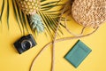 Flat lay traveler accessories on yellow background. Top view palm leaf, camera, rattan straw bag, pineapple and passport. Travel,