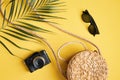 Flat lay traveler accessories on yellow background. Top view palm leaf, rattan straw bag, photo camera, sunglasses. Travel or Royalty Free Stock Photo