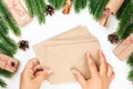 flat lay of two female hands holding stack of craft paper envelopes for greeting cards, Christmas background of fir Royalty Free Stock Photo