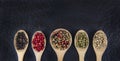 Flat lay of 5 types of peppercorn in a wooden spoon on a black background Healthy food concept