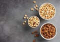 Flat lay of various types of nuts in white bowls on a gray concrete background