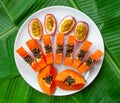 Flat lay. Vegetarian nutrition. papaya pieces and passion fruit on white plate with green banana leaves background, top view Royalty Free Stock Photo