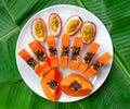 Flat lay. Vegetarian nutrition. Papaya pieces and passion fruit on white plate with green banana leaves background Royalty Free Stock Photo