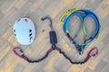 Flat lay of via ferrata gear white helmet, two lanyards with shock absorber system, climbing harness on wooden background.