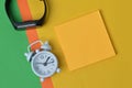 Flat lay view of a clock, watch, and a blank memo note over colorful background