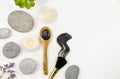 Flat lay view of mud charcoal mask on wooden spoon and smear on white background, surrounded with beauty brush and flat sea stones Royalty Free Stock Photo