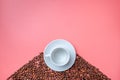 A white cup on a saucer stands on a hill of coffee beans on a pink background Royalty Free Stock Photo