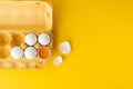 Flat lay of white eggs in the carton brown box on the yellow background. Top view of broken egg with white shell. Copy space for a Royalty Free Stock Photo