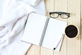 Flat lay of white knitted blanket, eyeglasses, cup of coffee and blank notebook paper on wooden background