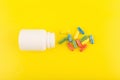 Flat lay with white medication bottle with spilled multicolored pills against yellow background