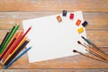 Flat lay of white Paper, watercolors, paint brush and colour pencils on wooden table Royalty Free Stock Photo