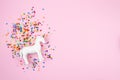 Flat lay with white unicorn and colorful glitter over the pink background. Magic surreal, fairy tale style. Minimal composition