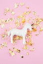 Flat lay with white unicorn and golden glitter over the pink background. Magic surreal, fairy tale style. Minimal composition