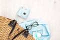 Flat lay woman handbag with elegant feminine accessories on wooden desk. Top view instant photo camera, glasses, gift box, blue