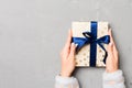 Flat lay of woman hands holding gift wrapped and decorated with bow on gray cement wooden background with copy space. Christmas Royalty Free Stock Photo