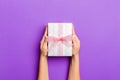 Flat lay of woman hands holding gift wrapped and decorated with bow on purple background with copy space. Christmas and holiday Royalty Free Stock Photo