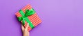 Flat lay of woman hands holding gift wrapped and decorated with bow on purple background with copy space. Christmas and holiday Royalty Free Stock Photo