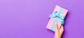 Flat lay of woman hands holding gift wrapped and decorated with bow on purple background with copy space. Christmas and holiday Royalty Free Stock Photo