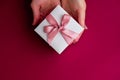 Flat lay of woman hands holding present with box decorated with pink ribbon on red background. Happy valentines day. Christmas Royalty Free Stock Photo