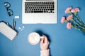 Flat lay woman office desk. Female hands with coffee and laptop, pink carnation, stationery on blue table. Top view