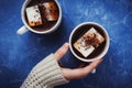 Flat lay of woman`s hands in sweater and two cups of cocoa or hot chocolate with homemade vegan marshmallow