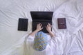 Flat lay of woman in white bathrobe with shower cap using laptop computer while lying down on her bed Royalty Free Stock Photo