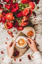 Womans hand holding cup of coffee over red flowers bouquet Royalty Free Stock Photo