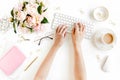 Flat lay women`s office desk. Female workspace with female hands, computer, pink peonies bouquet, accessories on white Royalty Free Stock Photo