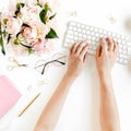 Flat lay women`s office desk. Female workspace with female hands, computer, pink peonies bouquet, accessories on white Royalty Free Stock Photo