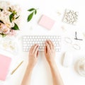 Flat lay women`s office desk. Female workspace with female hands, computer, pink peonies bouquet, accessories on white Royalty Free Stock Photo
