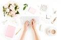 Flat lay women`s office desk. Female workspace with female hands, computer, pink peonies bouquet, accessories on white Royalty Free Stock Photo