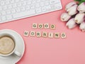 Flat lay of wooden letter GOOD MORNING on pink background with coffee cup, computer keyboard and purple-white tulip bouquet Royalty Free Stock Photo