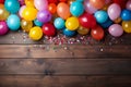 Flat lay of wooden planks with copy space surrounded by colorful party balloons, candy and confetti