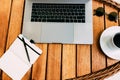 Flat lay of workspace for working at a laptop, on a brown wooden table with a cup of coffee and a notebook for recording cases.