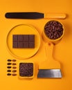 A flat lay on a yellow background featuring a chocolate bar, cocoa beans, cocoa nibs, and two spatulas. The image showcases Royalty Free Stock Photo