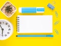 Flat lay, yellow office desktop with blank notebook and blue stationery, white clock, cactus. Top view with space for text. Royalty Free Stock Photo